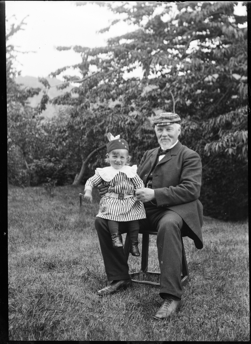 Christiane Liljefors far Roland Pedersen, sannolikt med sitt barnbarn Roland Liljefors, sitter ute i trädgård, sannolikt Norge omkring 1904-1905