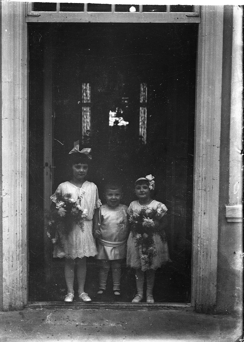 Två små flickor med en liten pojk emellan sig. De är klädda i ljus och flickorna håller en blomsterbukett i handen. De står sannolikt vid entrén till Ribbagården. Flickorn är möjligen syskonen Margit och Birgit von Otter