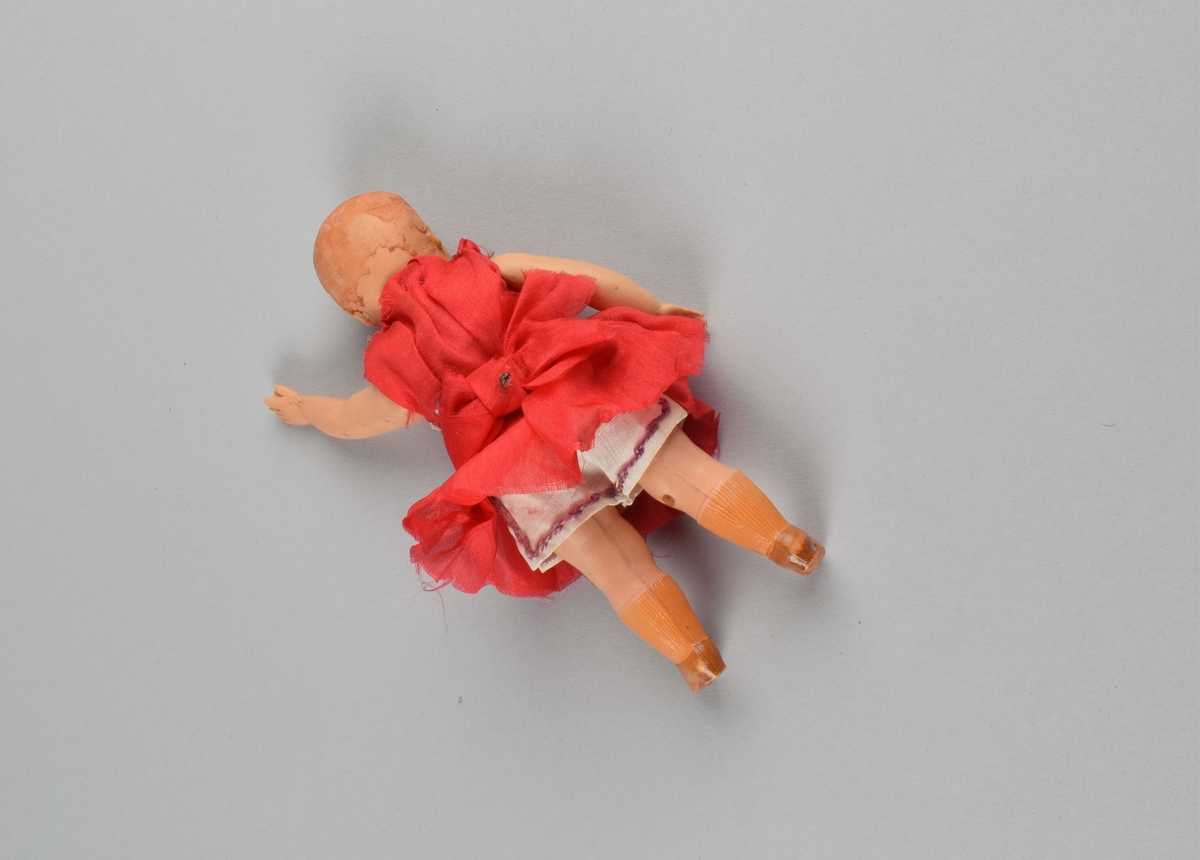 Liten figur av jente med rød kjole og hvite underbukser. Støpte sko og strømper. Bevegelige armer og ben festet med innvendig tråd.