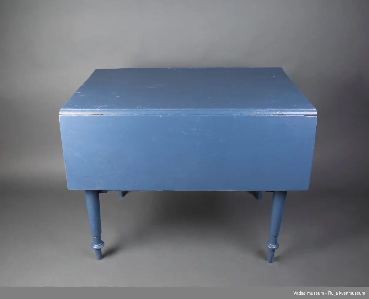 Rektangulært trebord med dreide bein. Bordet har hengslede sideklaffer. I ene kortenden er det en skuff med emaljert håndtaksknott. Bordet er malt i blått.