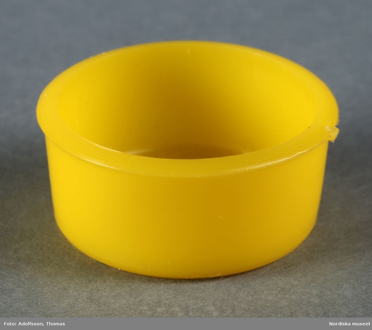 En rund tvättbalja av gul plast som hör till dockskåpsinredningen i källarens tvättstuga i dockskåp NM.0331721+.  Tvättbaljan står ovanpå tvättmaskinen (NM.0333458).