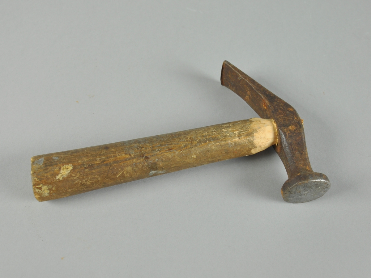 Skomakerhammer med hode av jern og skaft av tre. Banen er rund og uten skarpe kanter, mens pennen er skråstilt.
