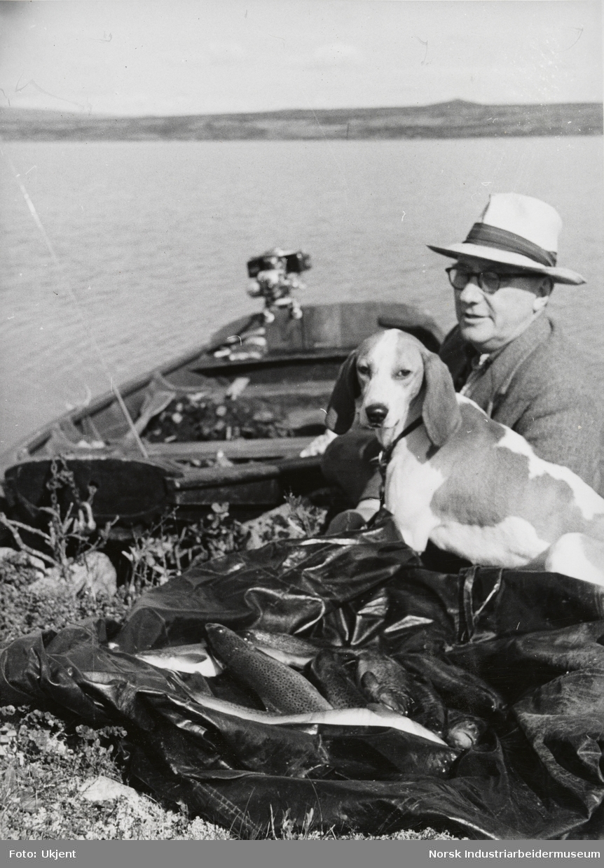 James Coward og hund ved robåt og fiskefangst ved innsjø