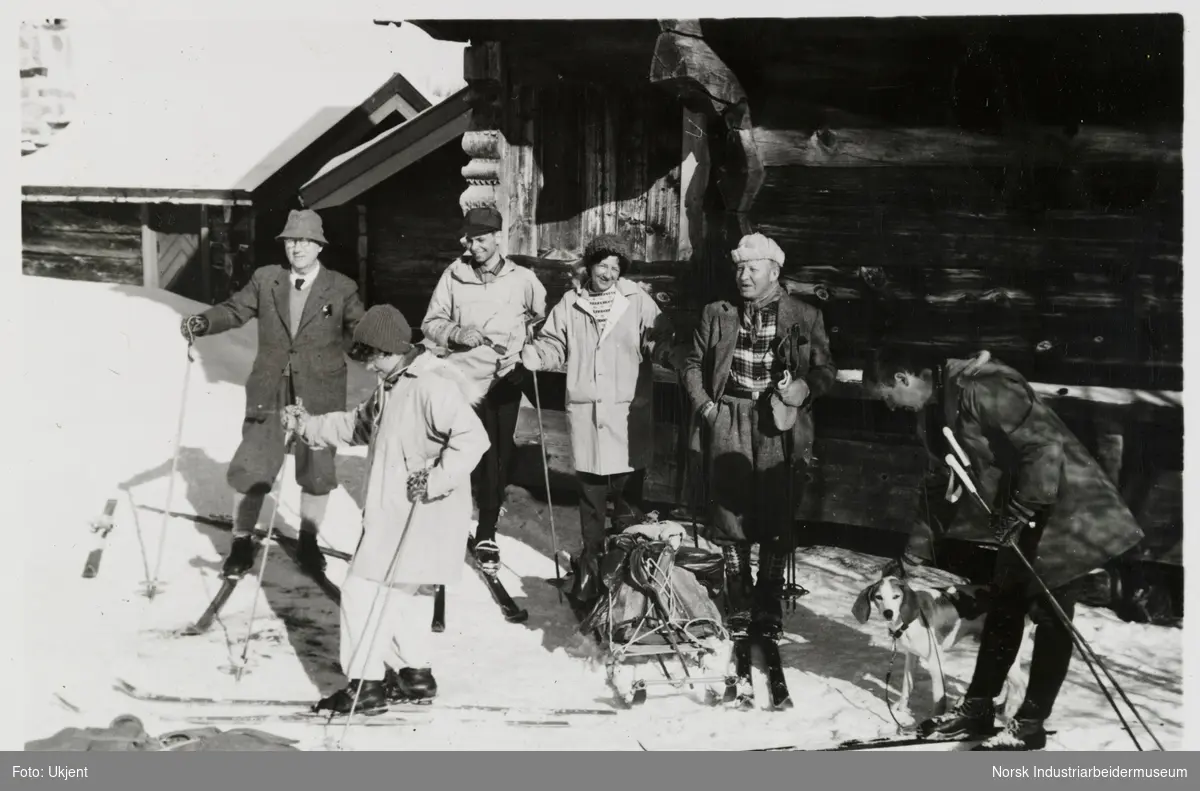 Mennesker i turklær på hyttetunet med ski og utstyr