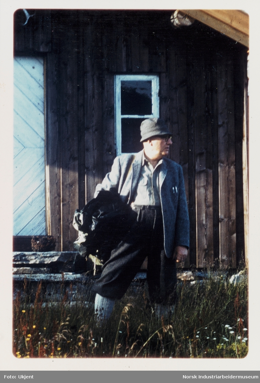 James Coward med jakke under armen står foran hyttevegg