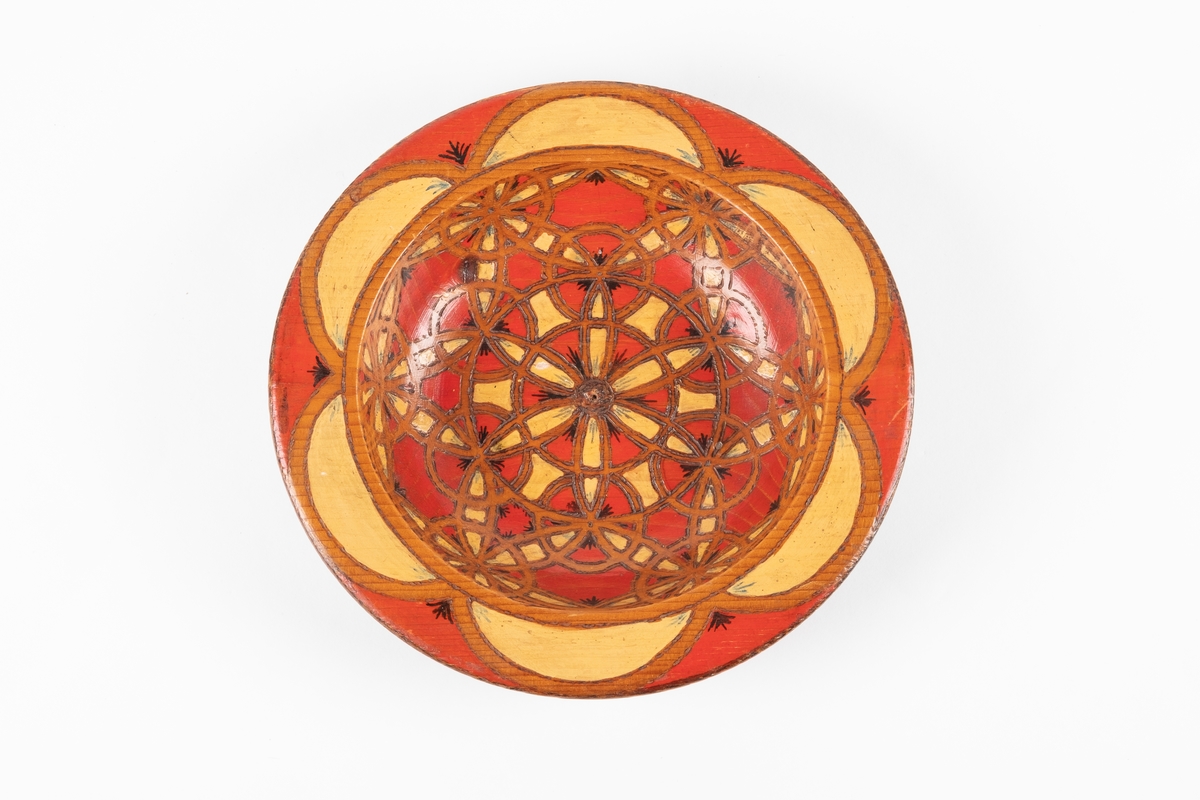 Trebolle med innbrent mosaikkmønster. Bollen er i rødt og gult på oversiden og brunt på undersiden. Det er påført tekst på undersiden.