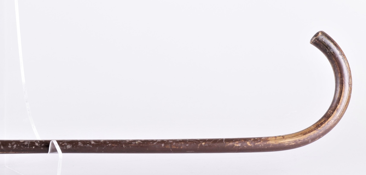 Spaserstokken er reparert med jernbeslag på midten. Mørkebrun farge, utenlansk tre, naturlig bøyd stokk. Initialer på håndtaket H W. (Hannibal Weidemann?)