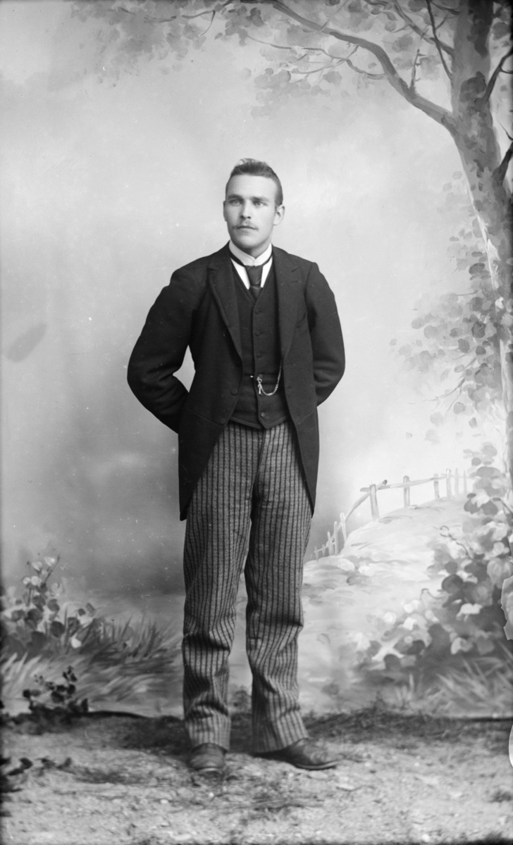 Atelierfoto av mann i mørk jakke og stripet bukse.