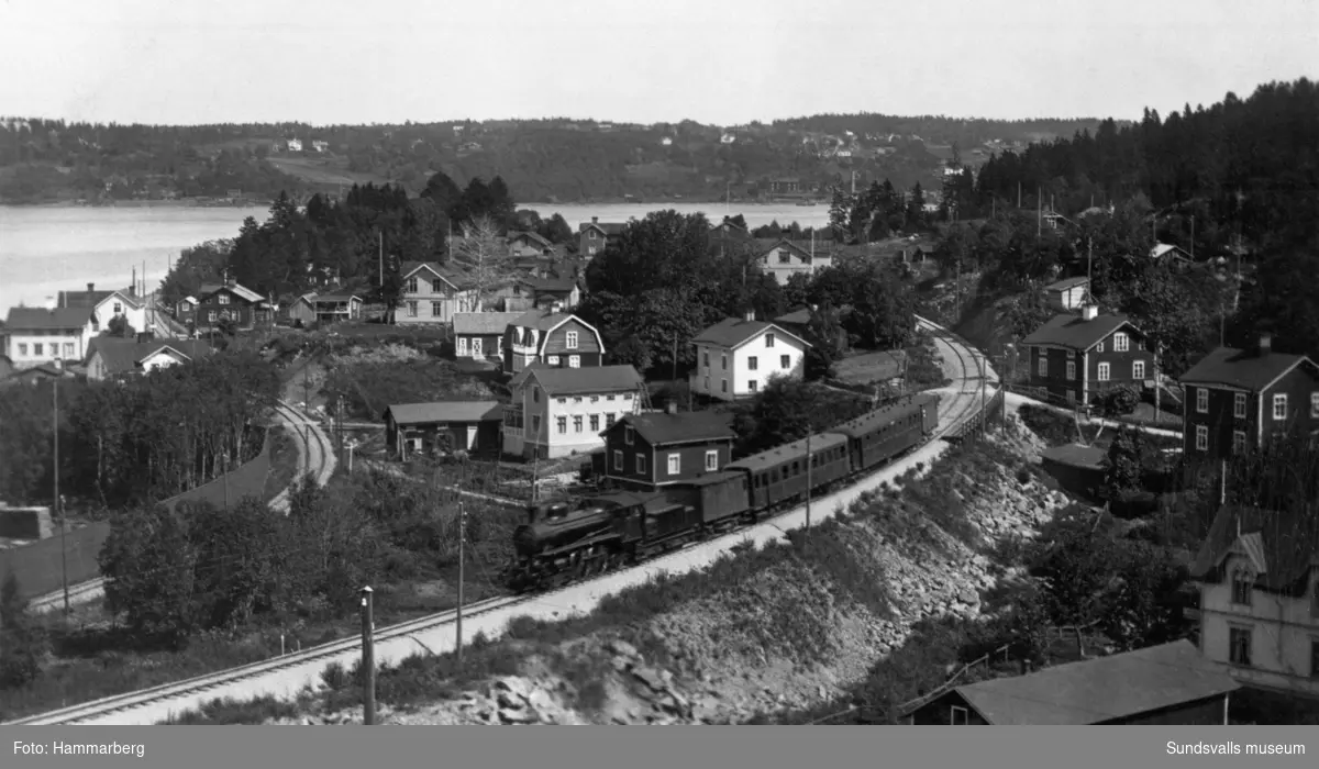 Ett ånglok med vagnar passerar Gångviken på Ostkustbanan, som invigdes 1927. Till vänster ses spårvägen Sundsvall-Skönvik (invigd 1925 och avvecklad 1952).