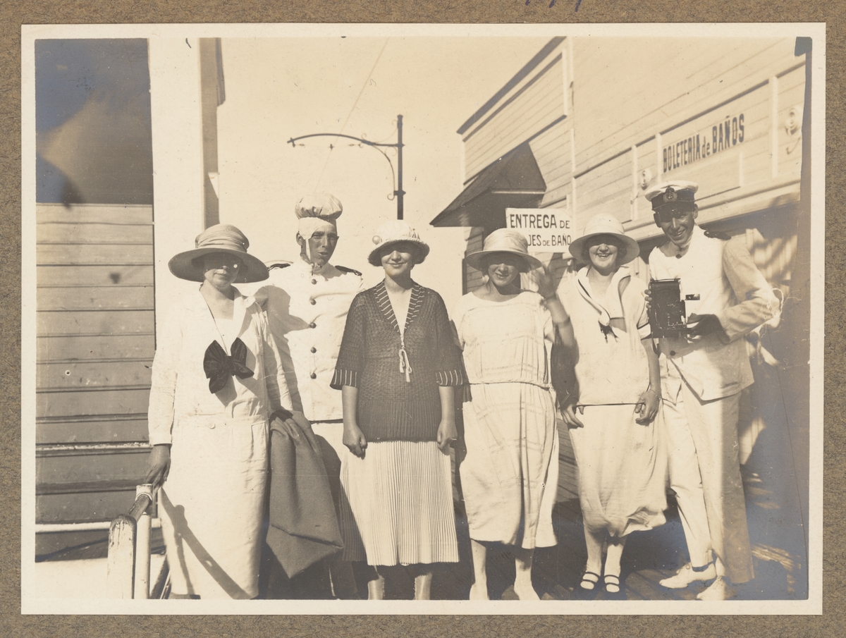 Bilden visar en grupp kvinnor med hattar som har tagit uppställning för fotografering på en badanläggning i Buenos Aires. Bredvid de står en svensk sjöman med en fotokamera.