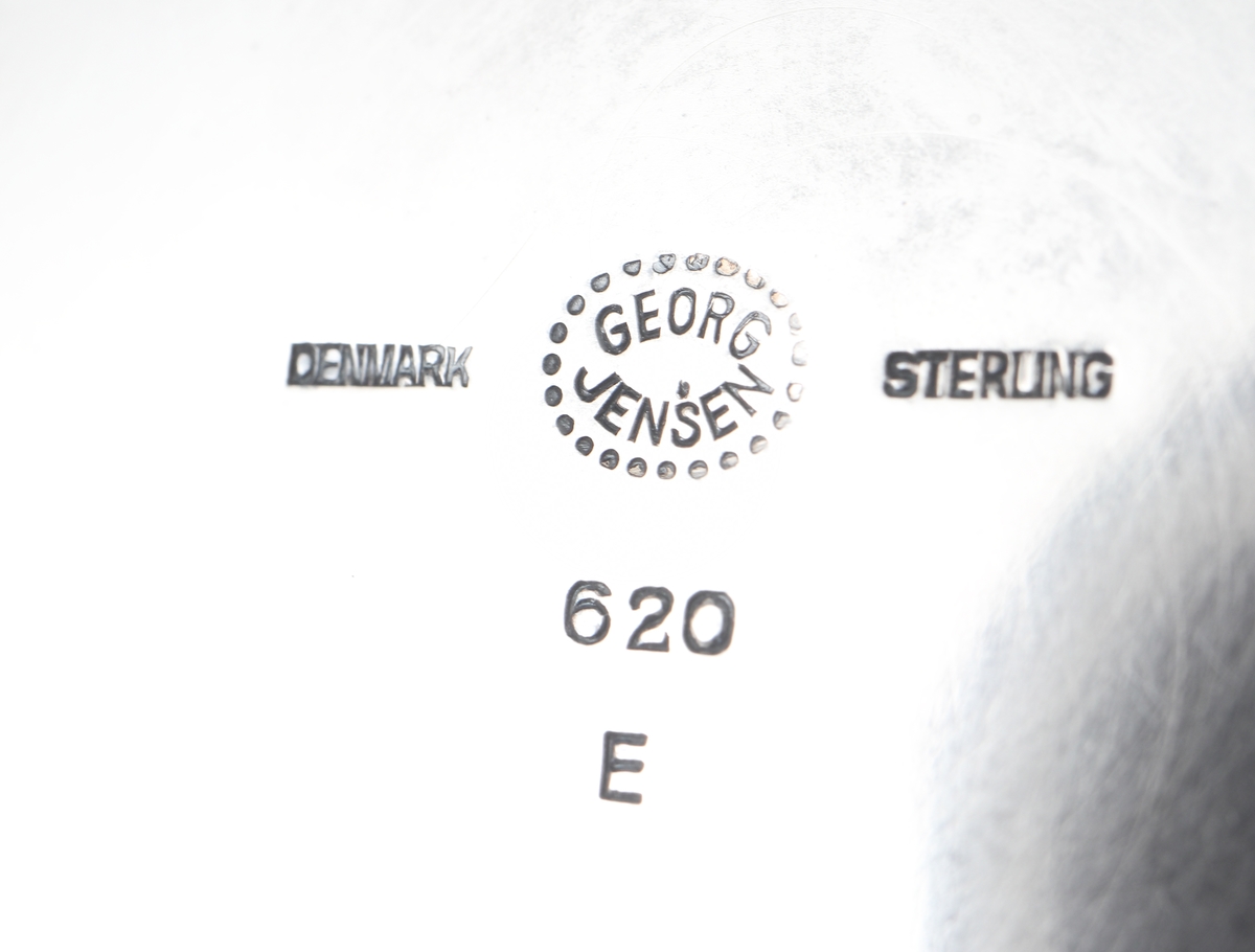 Fat av silver.
Rund, slät modell på låg, rund fot. På foten är graverat: "Fra Holmegaards Glasverk 8-9-1962". 
Inuti foten finns tillverkarstämpel m.m.