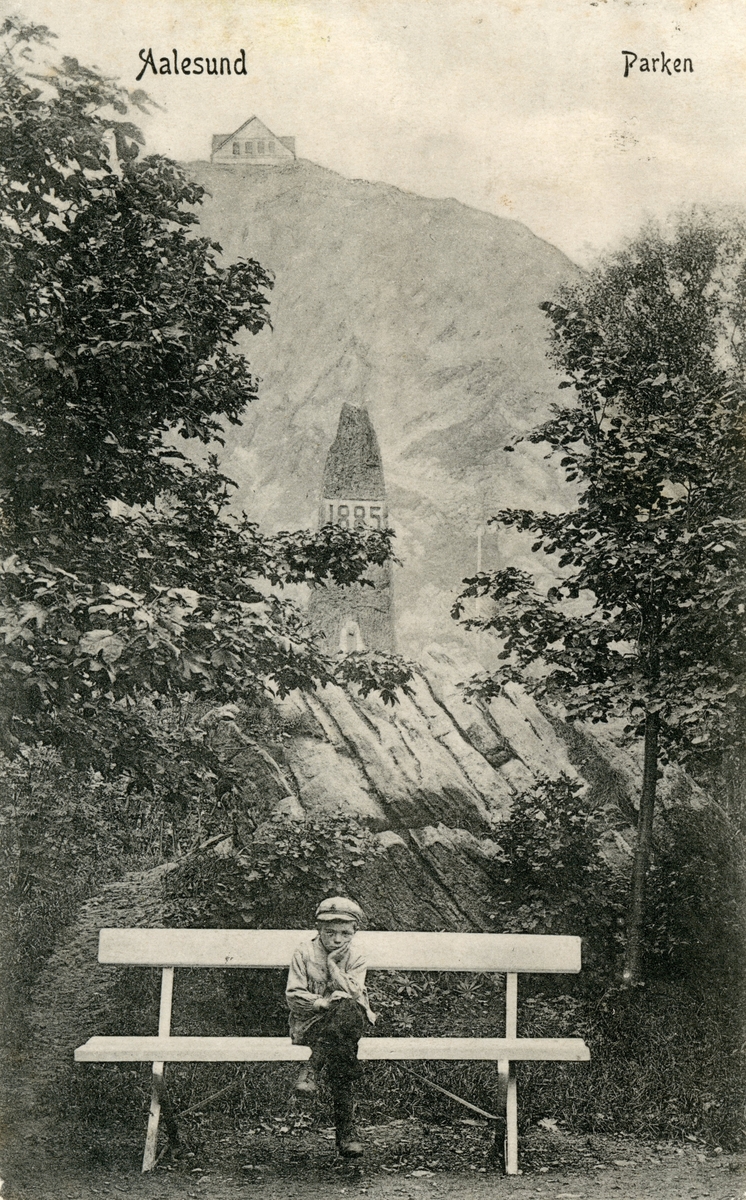 Motiv av en gutt som sitter på en benk i Ålesunds park. I bakgrunnen er en bauta med inskripsjonen 1885. Akslafjellet med Fjellstua lenger bak.
