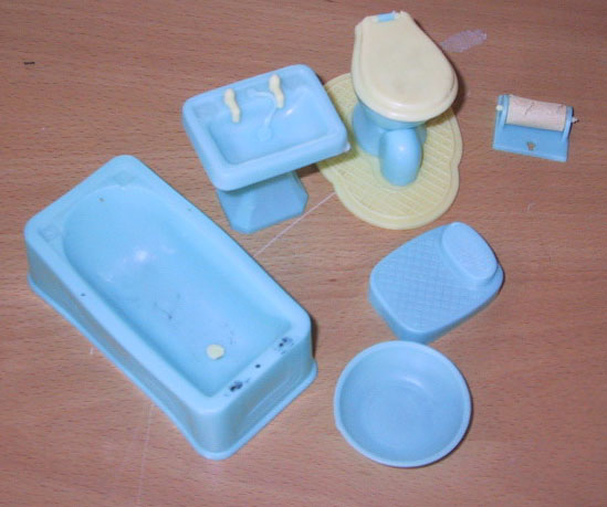 Blått og gult baderomsinventar i plast. Badekar, vask, badevekt, toalett med underlag, dorullholder og vaskefat.