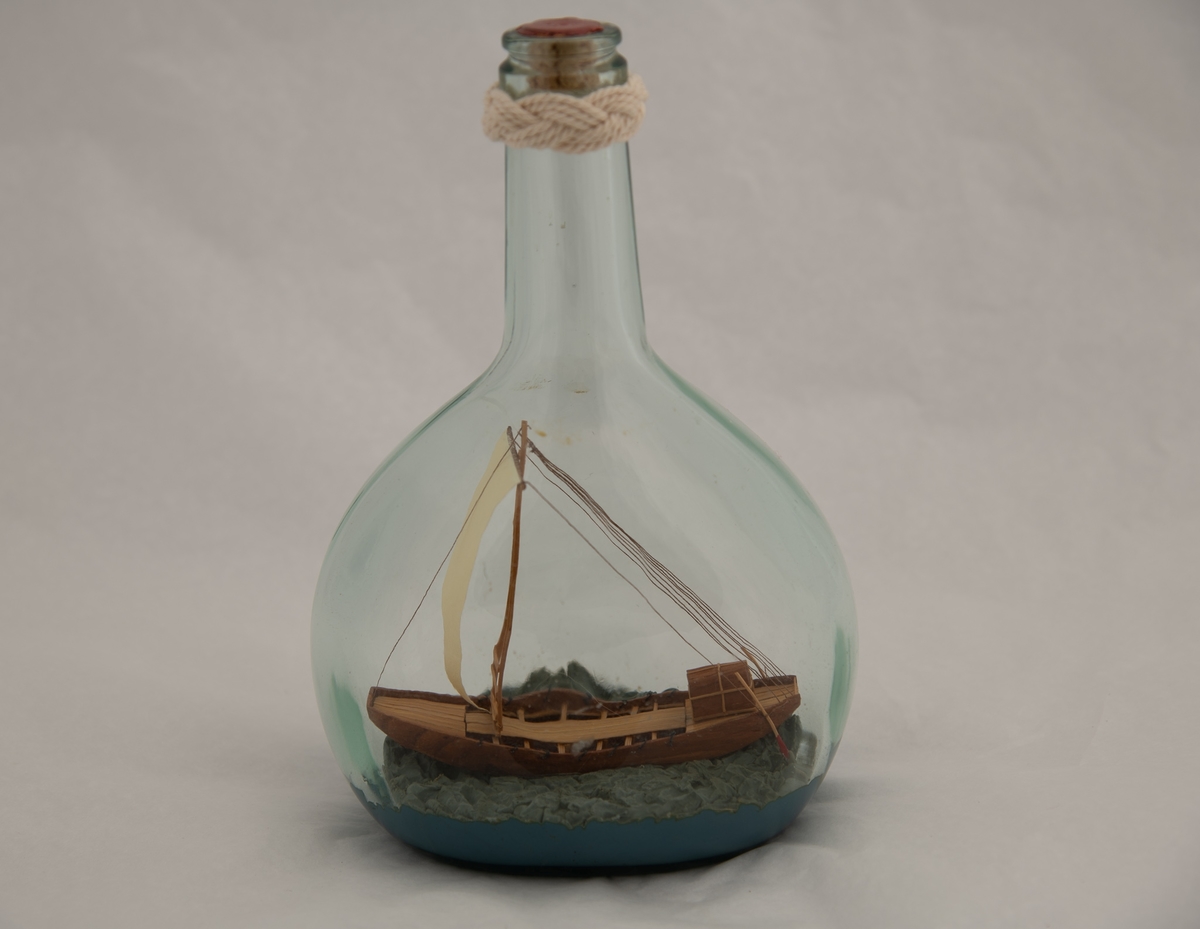 Flaskeskute: Egyptisk fartøy 1565-1080 f. Kr.  Flaske av klart glass (likørflaske) , innst. i bunnen 380 og g F. Oval bunn , flat på to sider , skrå skuldre , hals med en knop i seilgarn , munningen tettet med rød lakk. Bredbunnet skip , flatbunnet med trekantet seil , to styreårer bak og kahytt akter.