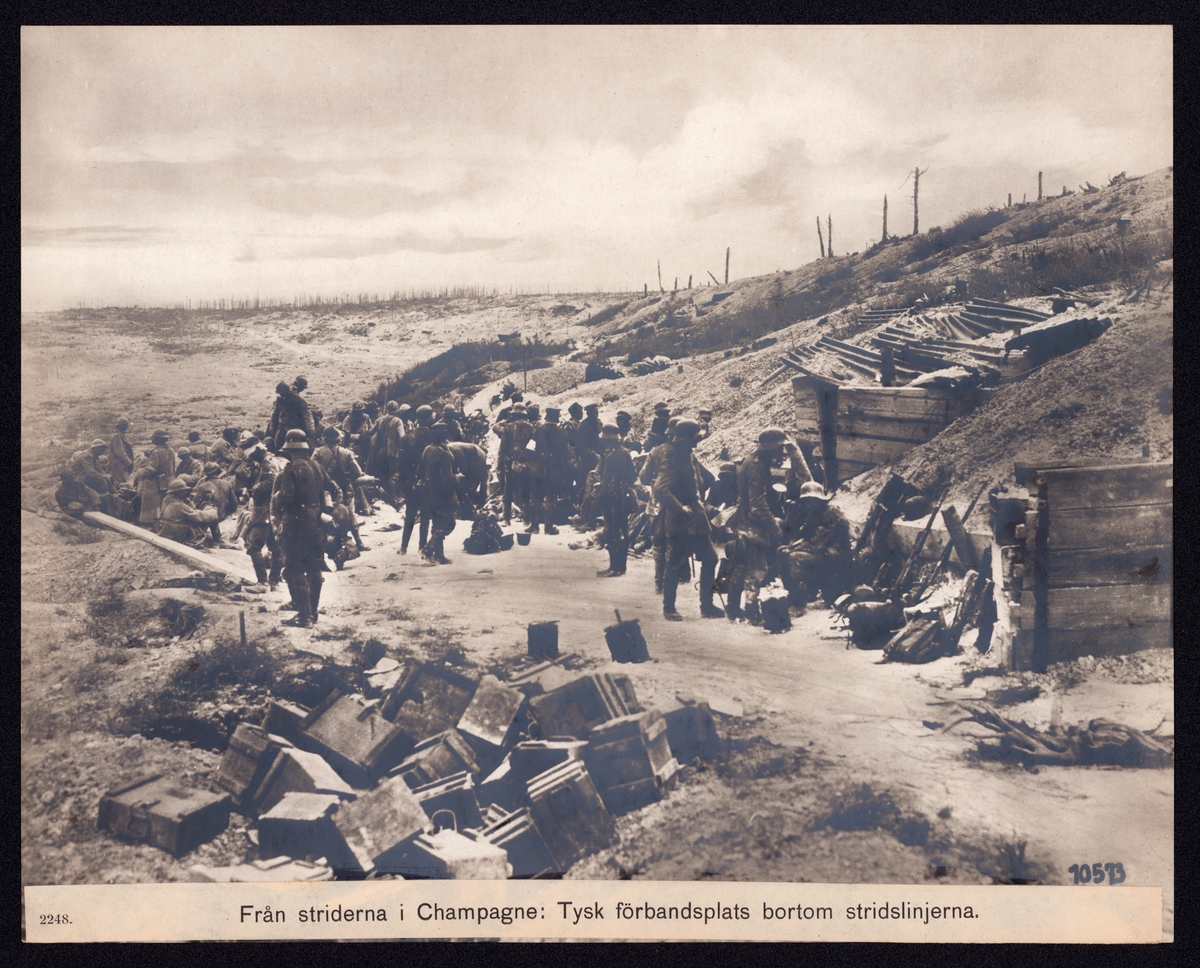 Bilden visar en öppen plats nedanför en befäst sluttning med tyska och allierare soldater. I förgrunden ligger en hög trälådor.