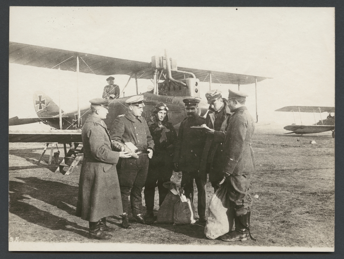 Bilden visar hur flera män i uniform hanterar postsäkar och dokument. I bakgrunden syn två dubbeldäckare flygplan.


Originaltext: "Flygofficeren mottager brevsäckarna och värdeförsändelserna."