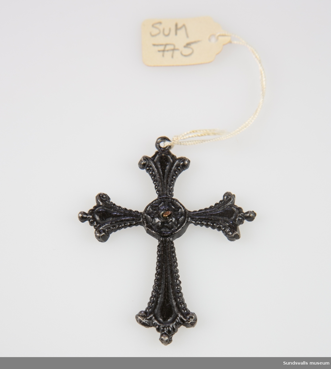 Hängsmycke i järn i form av ett kors i nygotisk stil med en kopparnit i mitten som kan ha hållit fast något på ena sidan av korset.