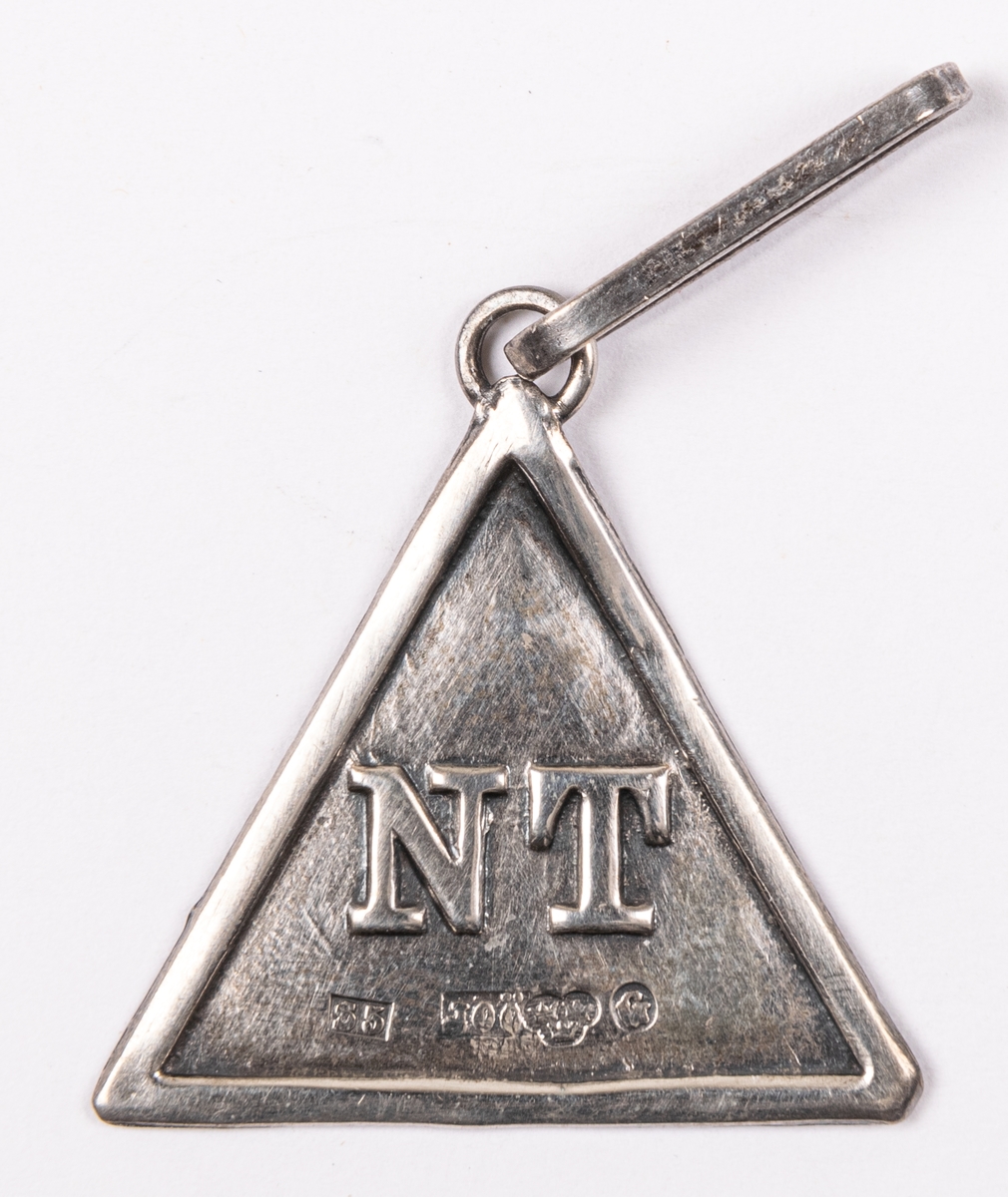 Ordensdekoration i silver, från Sällskapet NT, Gävle.
Triangelformat hänge med bokstäverna N T, samt silverstämplar:
S5 JOÖ kontrollstämpel G.