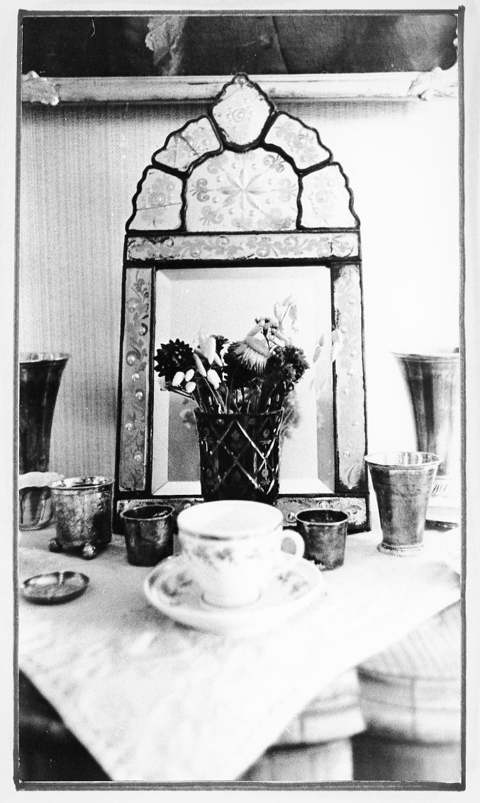 Interiör hos fröken Märtha Broomé på Gärdesvägen 38 i Gränna. Ett litet bord med tennbägare, kaffekopp, vas med blommor och en spegel.