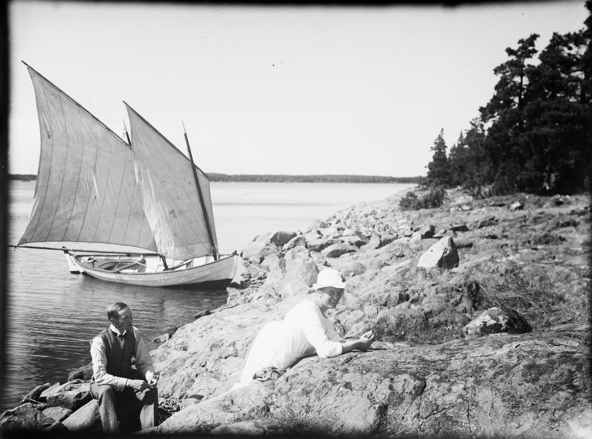 Skärgårdsvy - kvinna, man och segelbåt vid klippor, Östhammar, Uppland