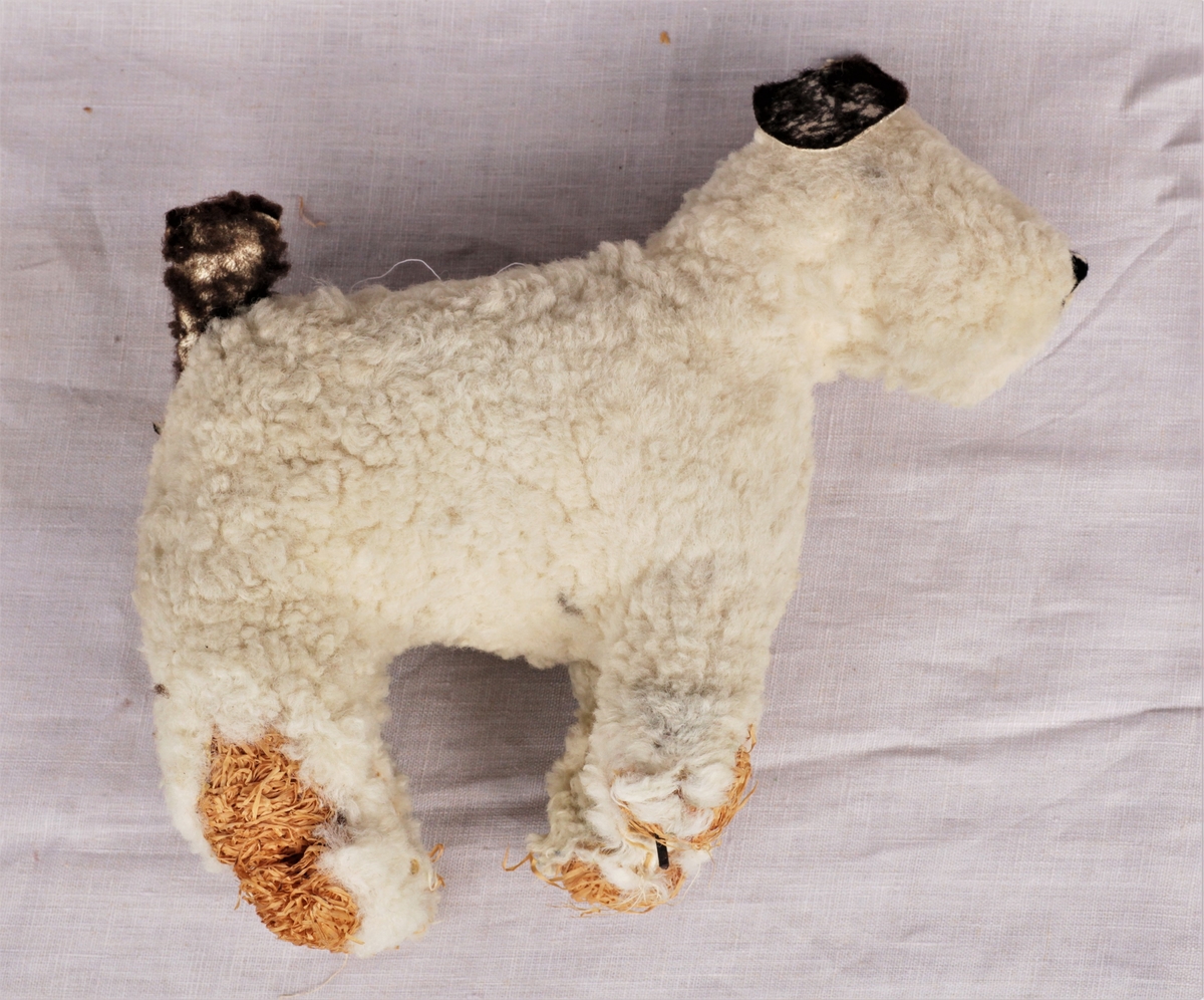 Hvit lekehund (terrier) med brune ører og brun hale. Metallramme og fylt med strå. En del slitasje på labbene, ørene og halen.