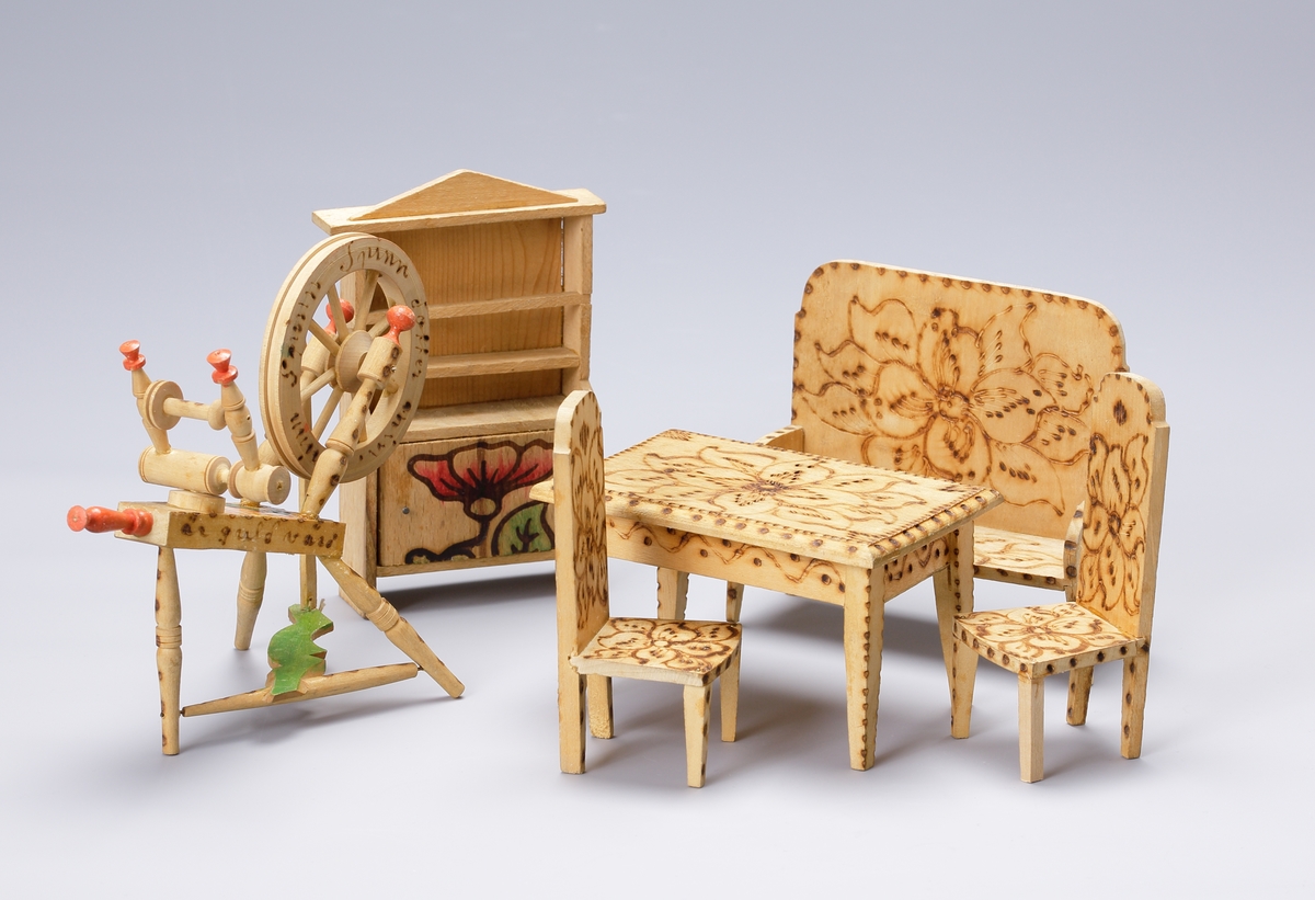 Dockmöblemang av trä, glödritat (med viss färgdekor i grönt och rött), bestående av ett bord, en soffa, två stolar, ett hyllskåp, en spinnrock och en nystvinda.