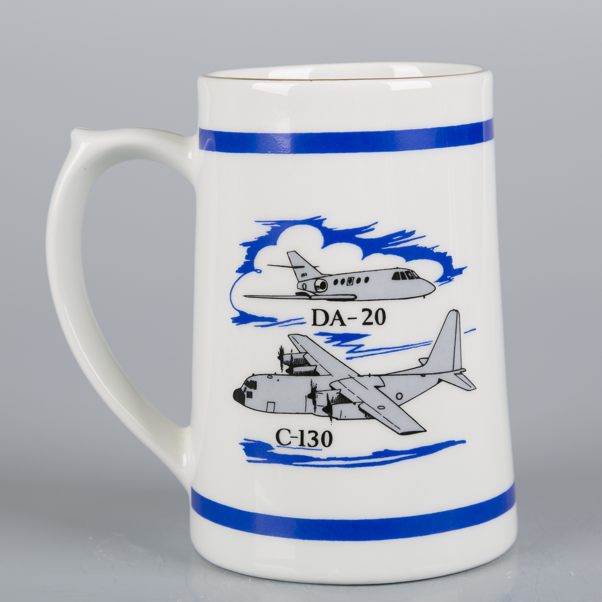 Krus med hank. Kronet logo. Bjelke øverst og nederst. Tegning av DA-20 og C-130.