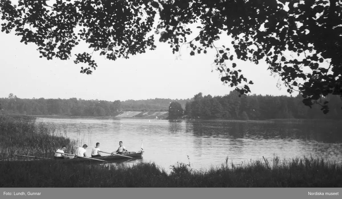 Motiv: Utlandet, Berlins Omgivningar 157 - 177 ;
Exteriör av en väderkvarn, landskapsvy med en sjö och skog - fyra män sitter i en kanot, en man och en kvinna sitter i en båt och matar en svan.