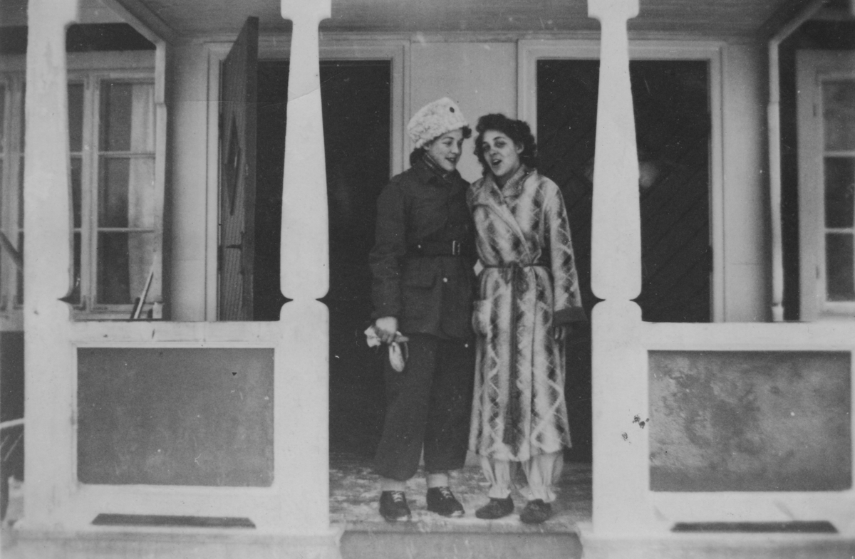 Porträtt av två kvinnor stående på verandan till luftbevakningsförläggningen i Tellejåkk, Kåbdalis, 91:a ls-kompaniet, 1942. Kvinnorna är luftbevakare. Till vänster: Karin Nordberg i uniform, till höger civilklädd Inger (efternamn okänt).