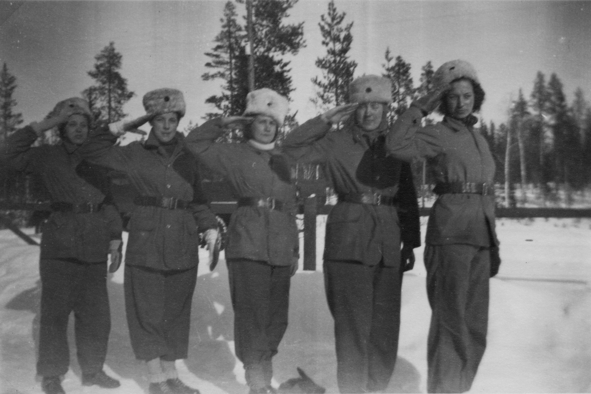 Porträtt av fem uniformerade luftbevakare som gör honnör, 1942. Från vänster; okänd, okänd, Birgit Johansson, Karin Nordberg och Sally Svensson. Luftbevakarna tillhörde 91:a ls-kompaniet vid luftbevakningsstationen i Tellejåkk, Kåbdalis under beredskapsåren.