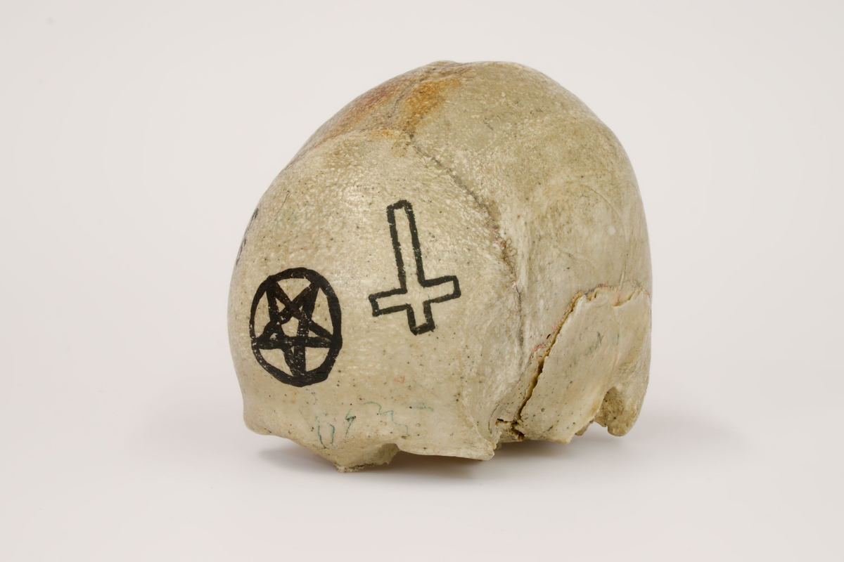 En ufullstendig menneskeskalle dekorert med okkulte symboler, en menneskeknokkel, (lårbein), to kors i metall, 6 tarotkort, en lang jernnagle.
