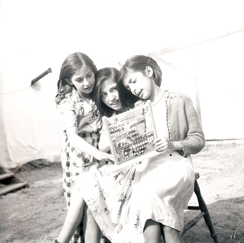 Fotografiet är taget i juli 1952 i samband med skolundervisning i det romska lägret i Ekeby, ca 4 km väster om Eskilstuna. Tre flickor sitter på en stol och räknar på en abakus.