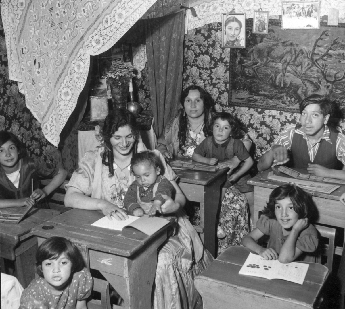 Romska barn och vuxna går i sommarskola 1943. I bänkraderna sitter barn och vuxna läsandes böcker. I bakgrunden syns draperier.
