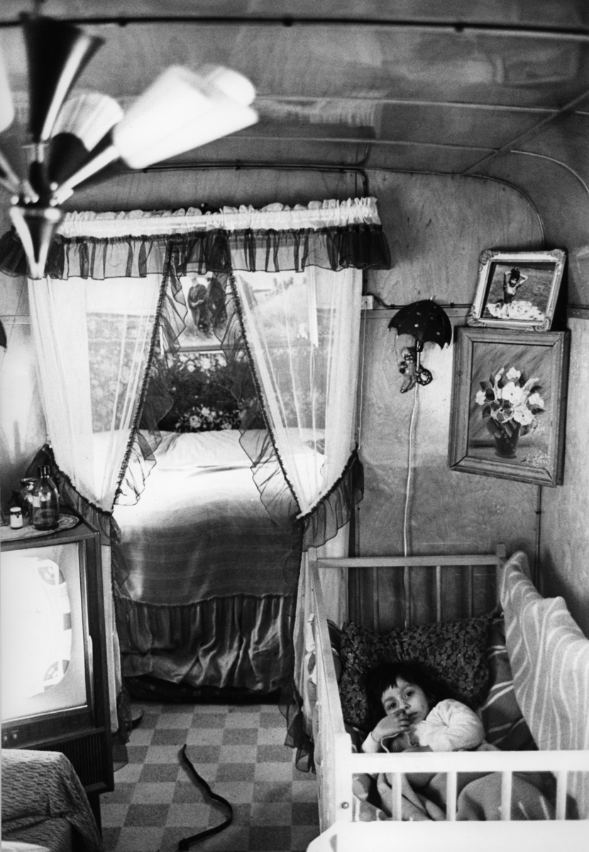 Romskt läger i Ekstubben 1963. En flicka ligger i en spjälsäng i en bostadsvagn.