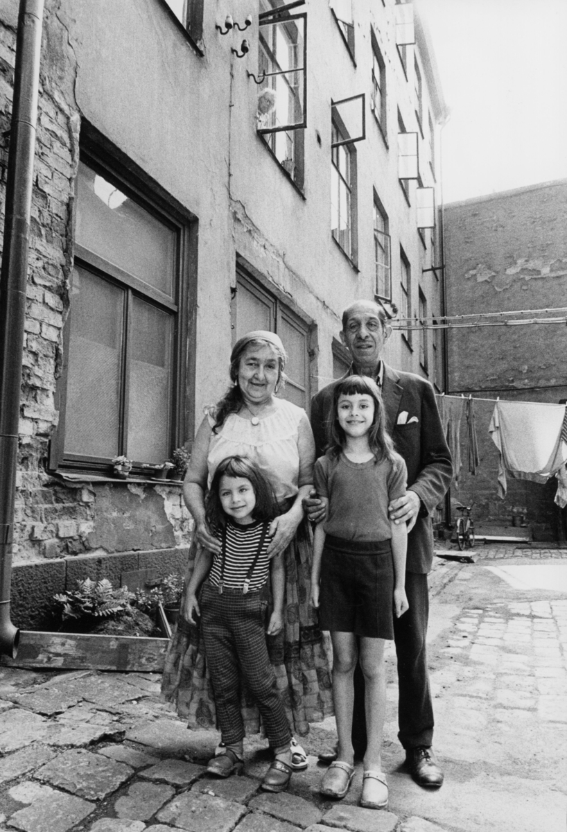 Morföräldrar med barnbarn i Stockholm 1972. De fyra står utanför ett lägenhetshus på en innergård. De vuxna står baom barnen.