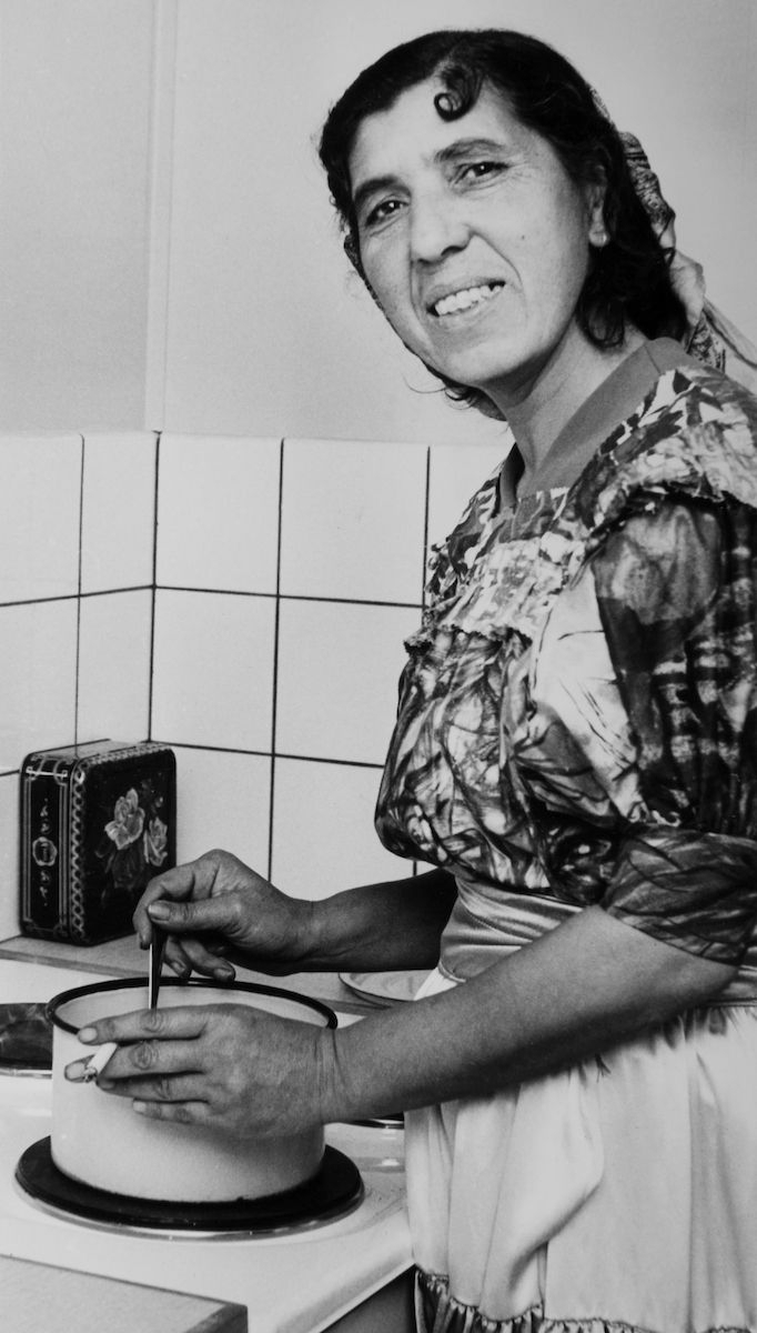 En kvinna står vid spisen och lagar mat. Bilden är troligen tagen i samband med att familjen fick tillgång till fast bostad. Efter att de svenska romerna i Sverige erkändes som medborgare år 1952 uppstod debatt kring gruppens svåra levnadsförhållanden. En statlig utredning genomfördes under 1954-1956 där en av slutsatserna blev att fast bostad var nyckeln till att lyckas med skolgång och arbetsliv. Från och med mars 1960 hade kommuner möjlighet att rekvirera statsbidrag för kostnader i samband med romers bosättning. Det lokala motståndet var dock stort och det tog flera år innan fast bostad kunde erbjudas till alla svenska romer.