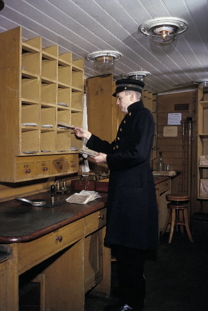 Seriebild ;M 25. I en ålderdomlig järnvägspostkupé, i
Järnvägsmuseum i Tomte-boda i Solna, arbetar en postiljon med
brevsortering. I den arrangerade situa-tionen agerar fotobiträdet
Gunnar Svensson, Postens Fotografer, i en uniform från Postmuseum.