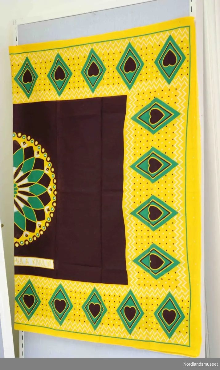 2 stykker skjal/sarong/kjole i bommullstoff påtrykt mønster i brunt, gult og grønt.
Det ene noe falmet på en del av stoffet.