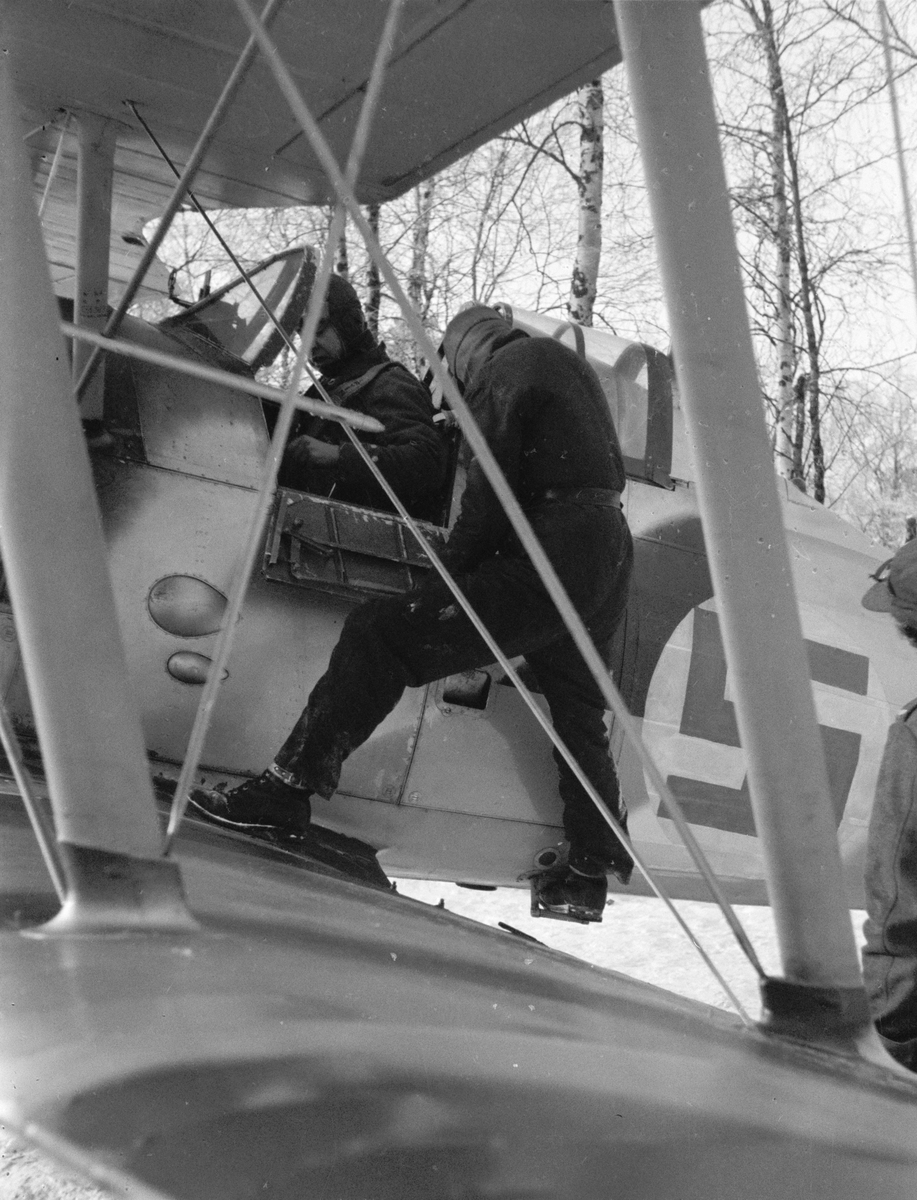 Istigning i flygplan Gloster Gladiator vid F 19, Svenska frivilligkåren i Finland, 1940. Flygförare får assistans av flygmekaniker. Vinge i förgrunden.