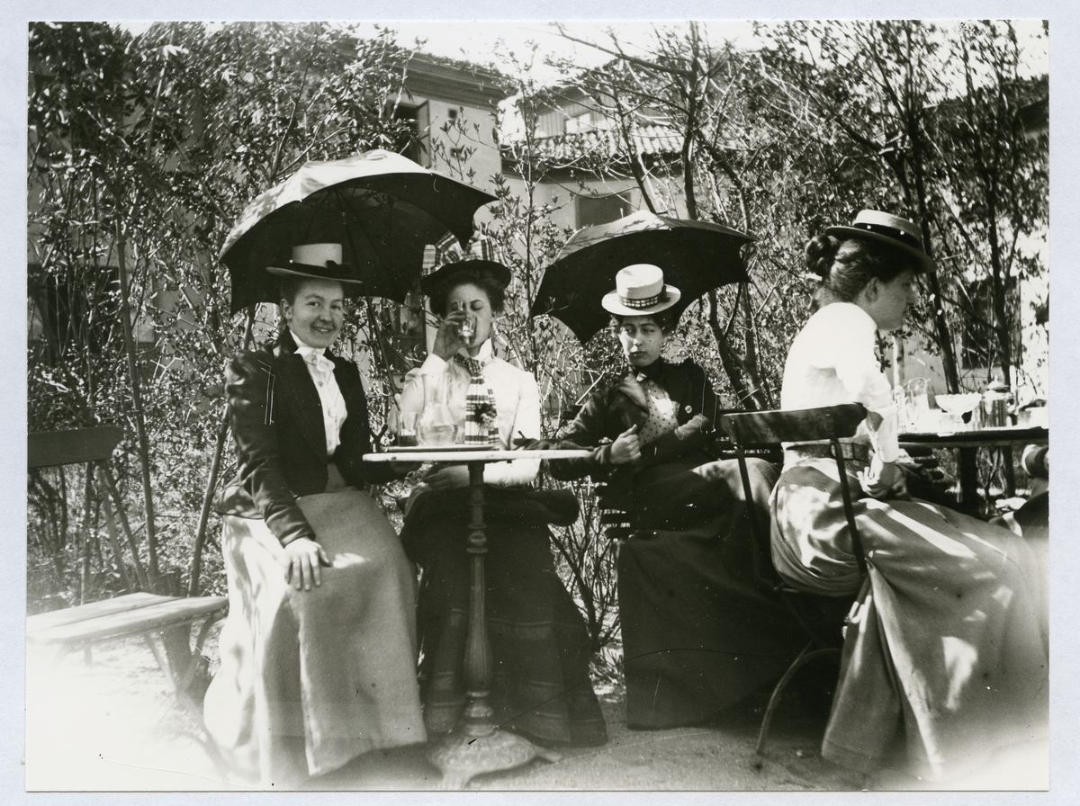 Stockholm. 
En grupp kvinnor sitter och fikar vid kafébord i trädgård. 1901.