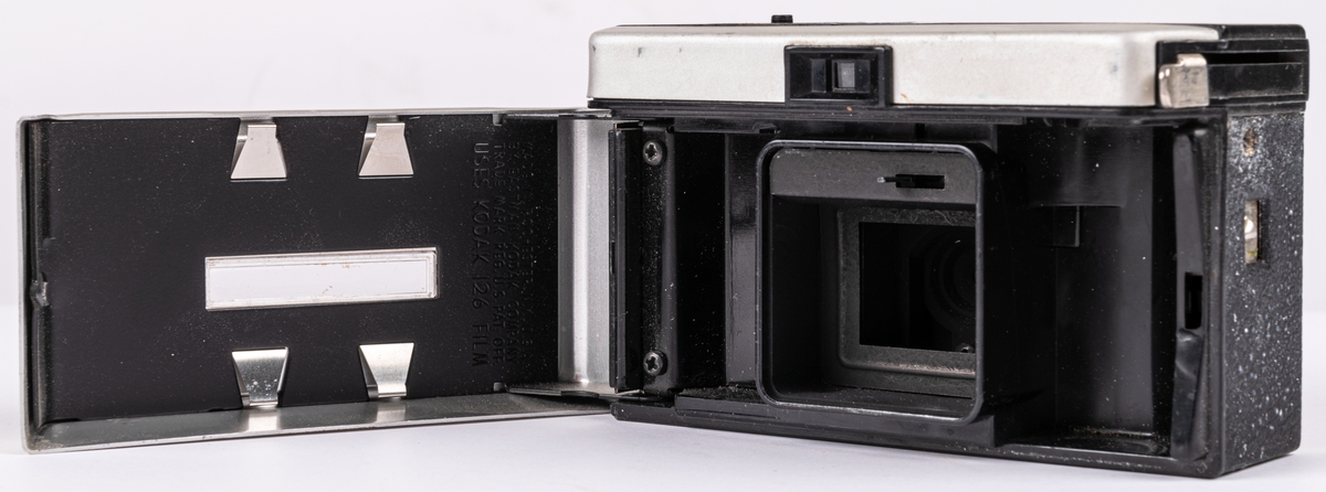Kamera, "Instamatic 104". Av grå "frostad" metall och svart, läderimiterad plast. Objektiv med räfflad kant. Sikthål överst i mitten. Uttag för blixtkub på ovansidan. I svart läderfodral med platt bärrem.