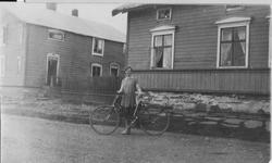 Dagmar Sundelin med sykkel foran Hallonengården med badstuby