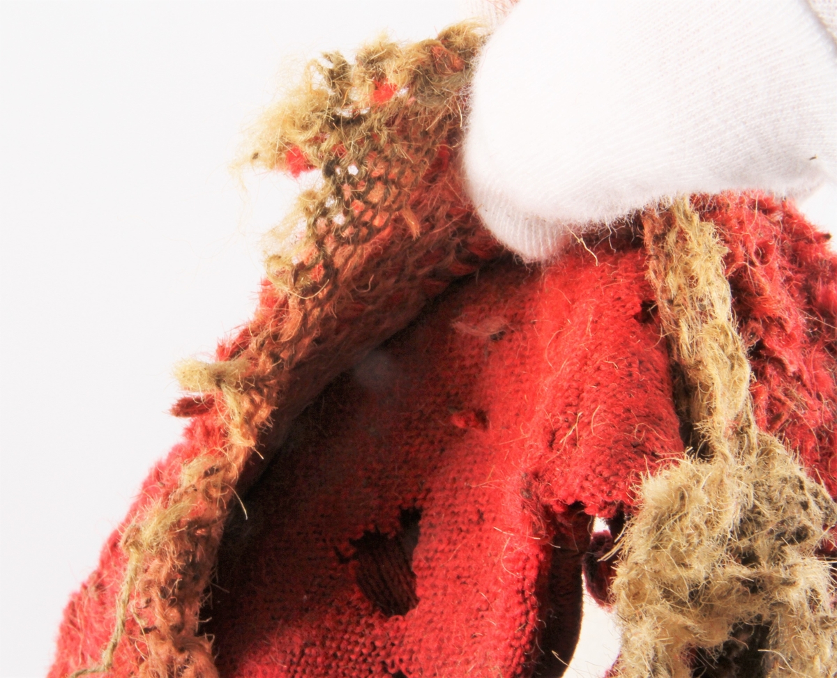 Rester av topplue strikket i høyrødt garn. Lua er glattstrikket fram og tilbake (5 masker pr cm) og er sammensydd i nakken. 7 cm dobbel kant med bukt øverst og antakelig også nederst. Brettekanten er festet ned med noen sting i forkant. Inni er kanten flosset med rød tråd. Antakelig har hele lua vært rød utenpå, men det er strikket fôr i hvitt (gulgrått?), her er maskene grovere og løsere. Selve lua kan være maskinstrikket. Kilde Ragnhild Bleken Rusten, Totn årbok 1994. Kommentar (RBR): Kan dette være et eksemplar fra Mykkby Manufakturen? Les bygdebok for Stor Elvdal av Fosvold. Manufakturen gikk under navnet "Enigheten".