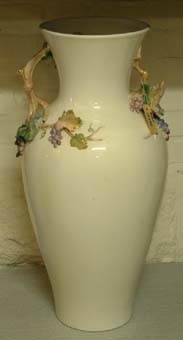 Urna av vitt porslin med dekor av vinrankor som även till viss del bildar två handtag upptill.
Färgerna är huvudsakligen i blått, ljusgrönt och gulbrunt.