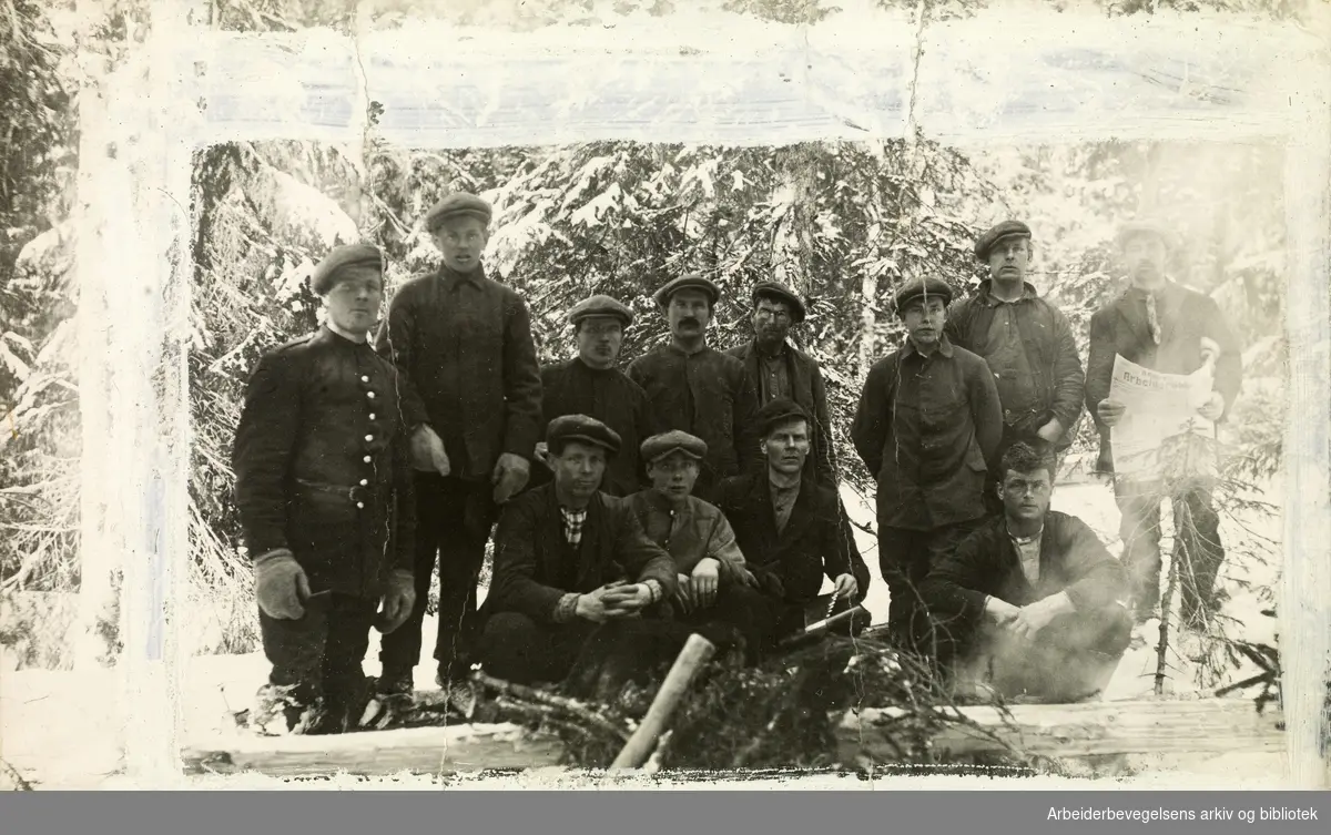 Tømmerhoggere fra Namdalen. Mannen til høyre i bildet holder et eksemplar av Namdalen Arbeiderblad. Vinter. .Ikke tidfestet. .