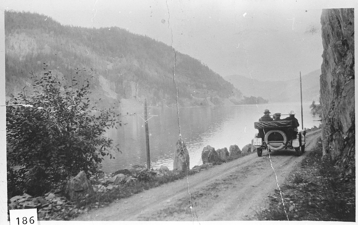 Norefjord, 1923. Vei langs fjorden med stabbesteiner. Åpen bil sett bakfra. 3 personer i bilen. Registreringsmerke F-225. Bilen tilhørte lensmann John Kopseng.