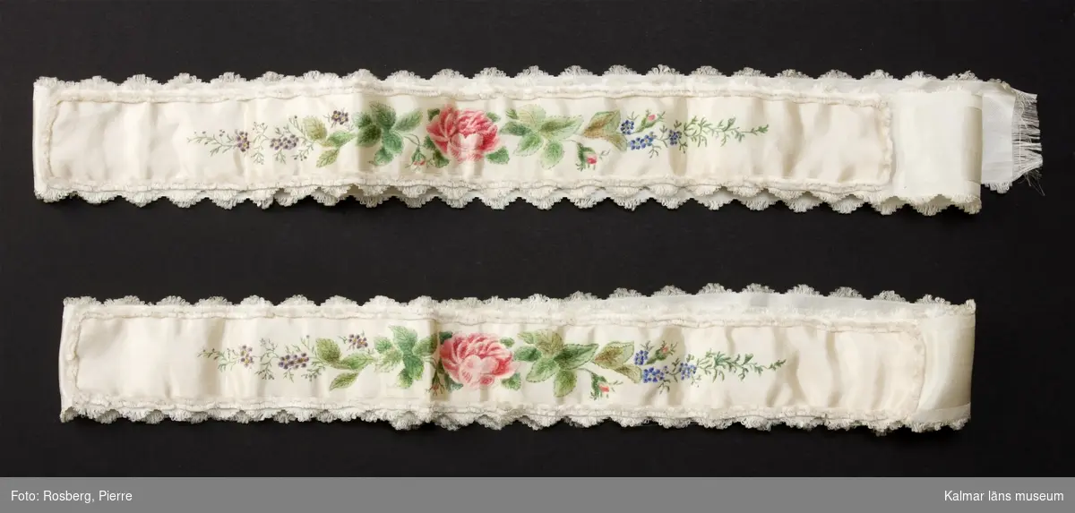 KLM 39661:130 Brudstrumpeband av siden. Dekorerade med målade blommor på vit sidensatäng. På tillhörande papperslapp text: Min Mammas brudstrumpeband och näsduk. Näsduken medföljde inte gåvan.