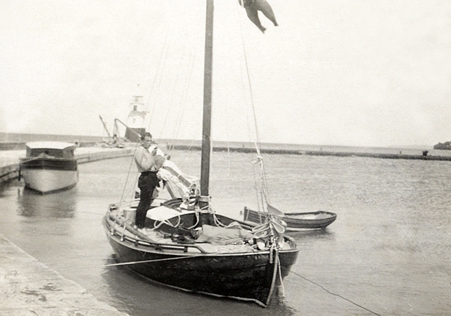 En ung man med pipa i hand, på en segelbåt förtöjd i hamn.