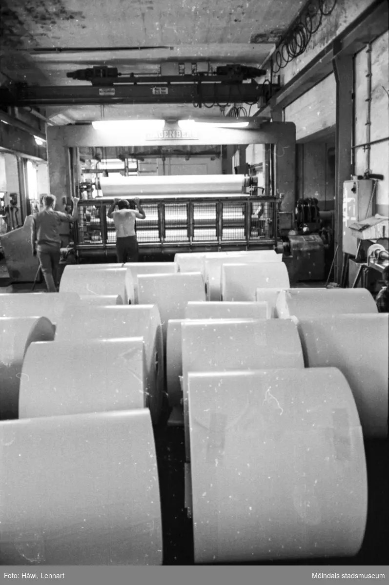 Män i arbete vid maskin, rullmaskin 5. Färdiga rullar från rullmaskinen. Byggnad 10. Pappersbruket Papyrus i Mölndal, hösten 1970.