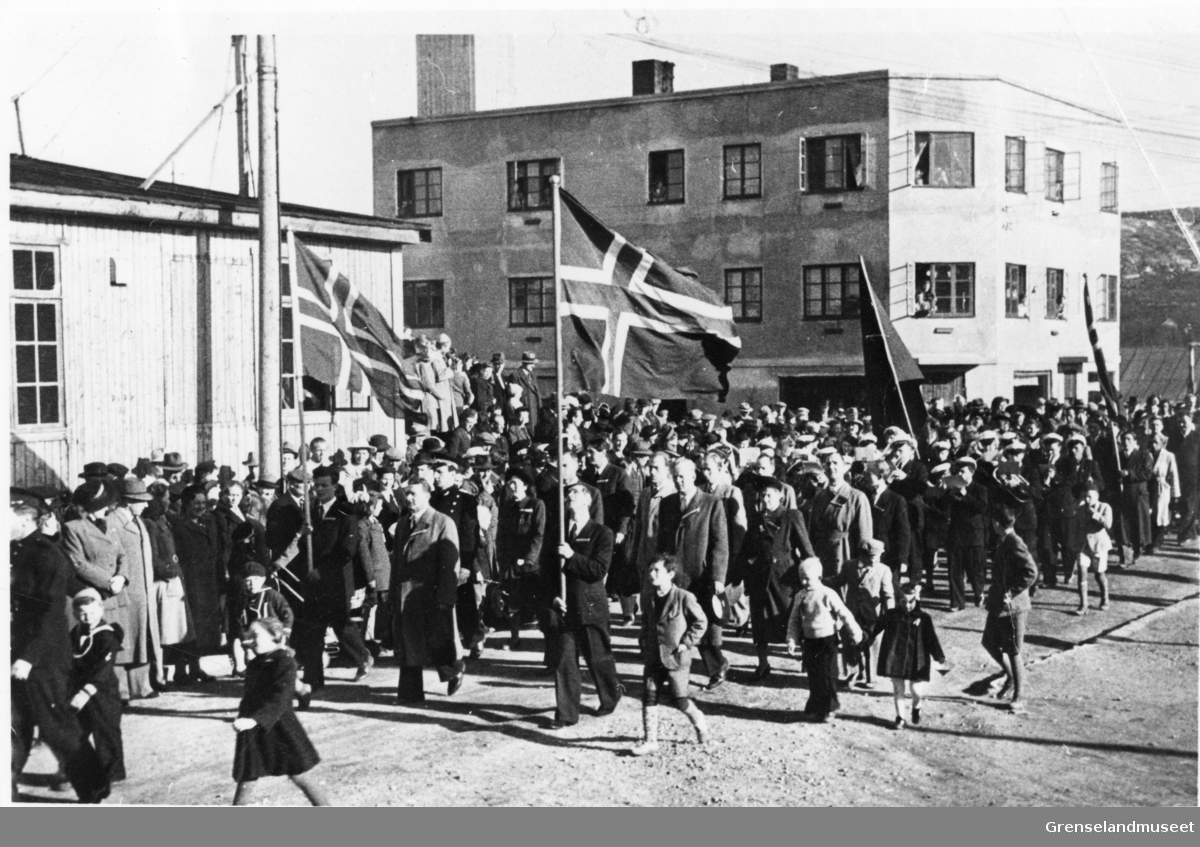17. mai tog opp Toklebakken i Kirkenes 1945, betongskolen i bakgrunnen. Bak flaggborgen Jonas Madsø, politi.